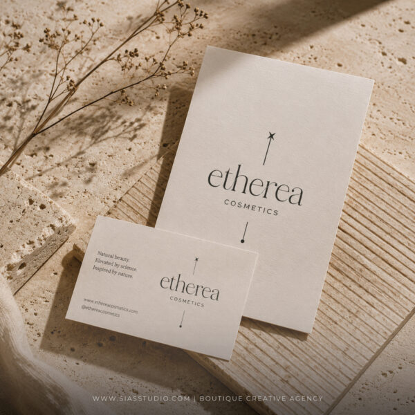 Logo Etherea Cosmetics applicato su materiali coordinati in carta materica, ambientati su travertino beige con elementi botanici